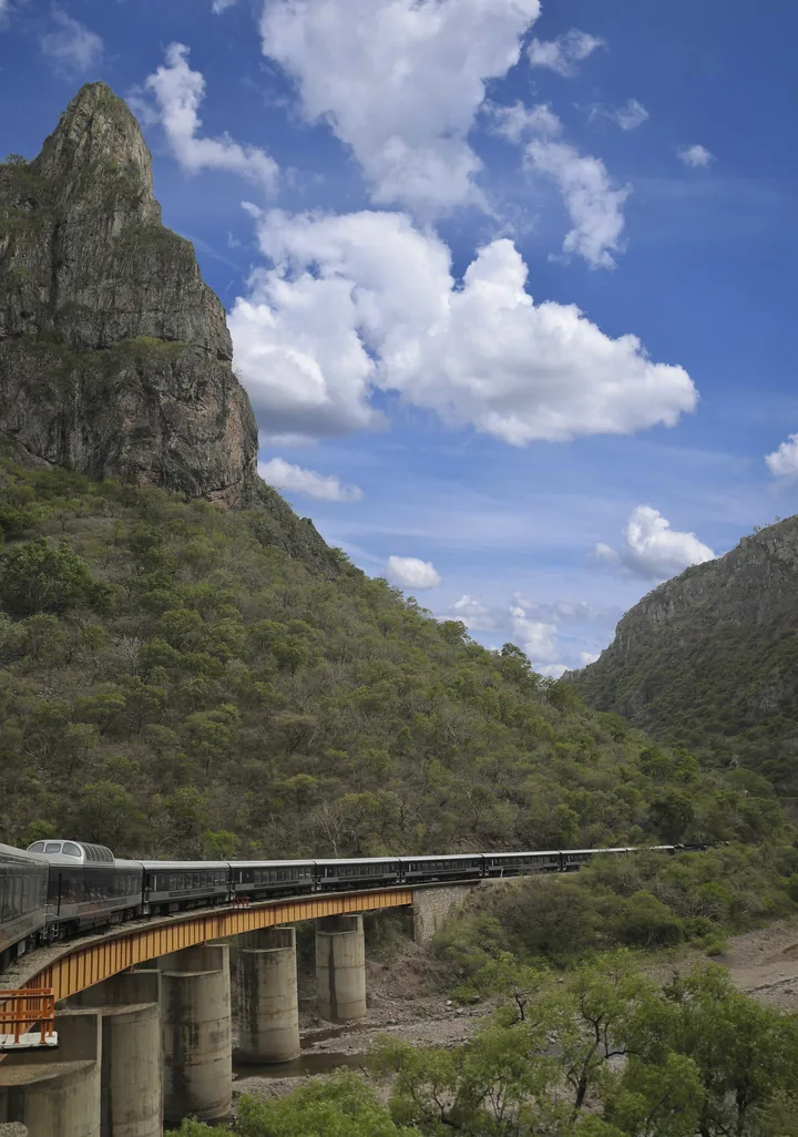 Tren con vagón panorámico cruzando un puente sobre una barranca