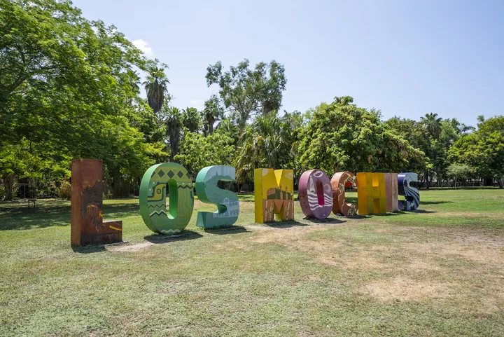Letras monumentales de Los Mochis decoradas con motivos locales, instaladas sobre el césped de un parque arbolado