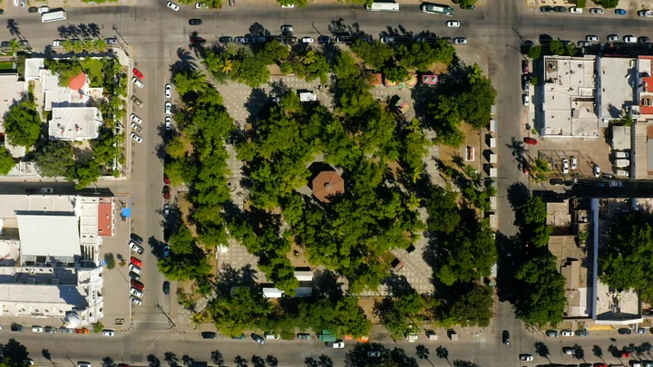 Vista aérea cenital de una plaza urbana arbolada con kiosco central rodeada de calles y edificios